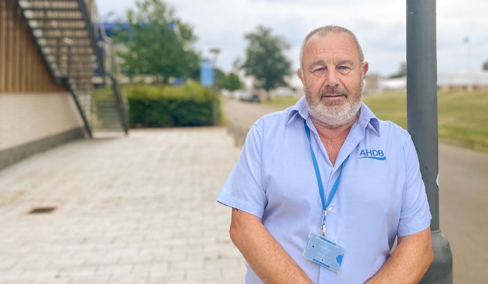 A man (Pat Loten) wearing a short sleeved light blue shirt leaning against a lampost